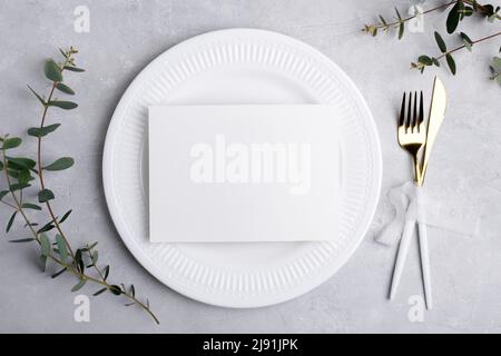 Wedding stationery invitation card mockup 7x5 on white classic plate on grey background with eucalyptus, Menu card mockup with festive wedding or birt Stock Photo