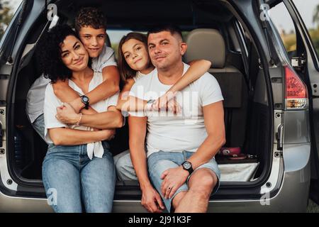 Portrait of Happy Four Caucasian Members Family Sitting in Trunk of the Minivan Car, Mother and Father with Two Teenage Children, Son and Daughter