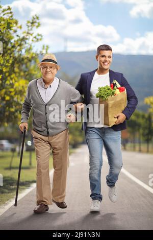 Young man helping an elderly man with a grocery bag and walking on a pedestrian lane Stock Photo
