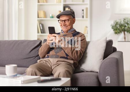 Elderly man smiling and using a smartphone seated on a sofa at home Stock Photo