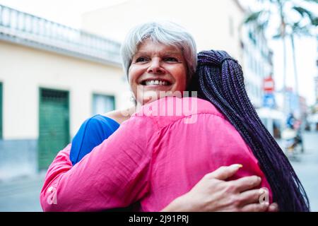 Multiethnic senior women hugging each other - Elderly diverse community concept - Focus on caucasian female face Stock Photo