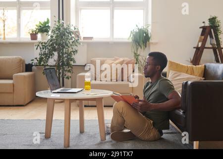 Side view shot of young adult African American man spending time at home sitting in front of laptop having video call with general practitioner Stock Photo