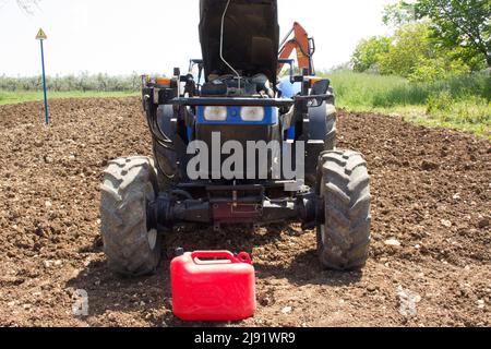 Image of a tractor parked in a field with a rubber hose and a can while sucking diesel from the tank. Reference to the theft caused by expensive fuel. Stock Photo