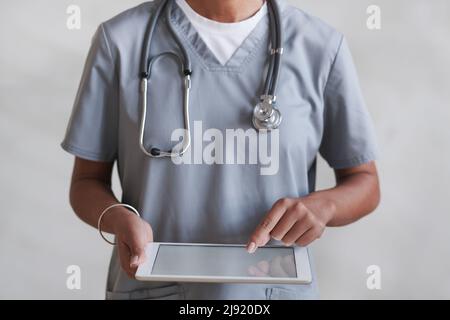 Medium section studio shot of unrecognizable female doctor wearing gray uniform using digital tablet Stock Photo