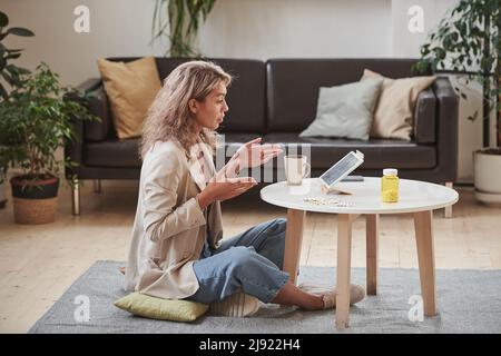 Horizontal side view shot of modern young adult woman sitting in front of digital tablet talking to doctor online Stock Photo