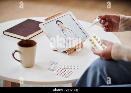 Unrecognizable woman having online appointment with doctor using digital tablet holding pills and thermometer Stock Photo