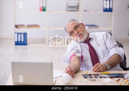 Old male drug addicted employee sitting at workplace Stock Photo