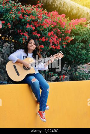 A girl sitting playing guitar outdoors, Portrait of a smiling girl playing guitar, Lifestyle of a girl playing guitar outdoors Stock Photo