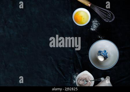 eggs and egg shells on a dark background surrounded by bowls and a whisk Stock Photo