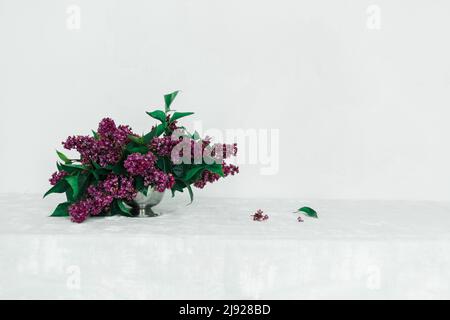 Lilac flower arrangement on a table with a gray tablecloth against a white wall Stock Photo