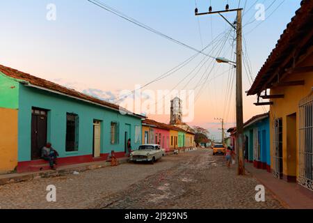 Picturesque street scene after sunset, cobblestones, telegraph pole with power lines, people, Cubans sitting in front of the front door, classic car Stock Photo