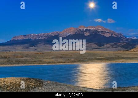 full moon setting behind sawtooth ridge and a prairie pond along the rocky mountain front near choteau, montana Stock Photo