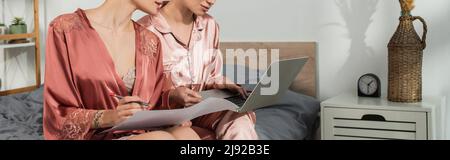 partial view of young bigender lovers working with laptop and papers in bedroom, banner Stock Photo