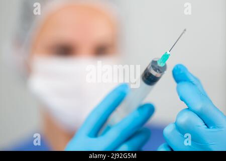 Masked female healthworker prepared a syringe for injection, filling it with medicine Stock Photo