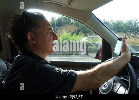 20.08.2021, Berka, Thuringia, Germany - Man looking at his cell phone during a car ride. 00S210820D599CAROEX.JPG [MODEL RELEASE: NO, PROPERTY RELEASE: Stock Photo