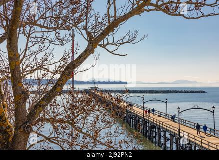 Wooden pier at White Rock, BC extends diagonally into image. Beach and pier at sunset, Surrey, BC, Canada-February 22,2022-Travel photo, selective foc Stock Photo