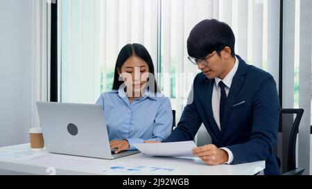 Two asian business people are working together and analyzing the data on the computer. Stock Photo
