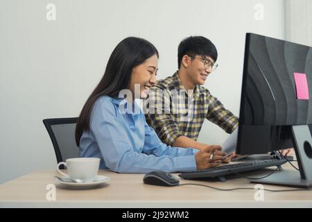 Young asian partner programmers working in team while making a new computer codes on desktop computer in the office. Stock Photo