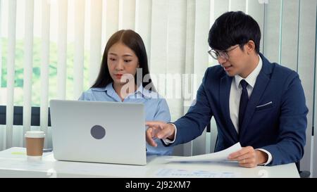 Two asian business people are working together and analyzing the data on the computer. Stock Photo