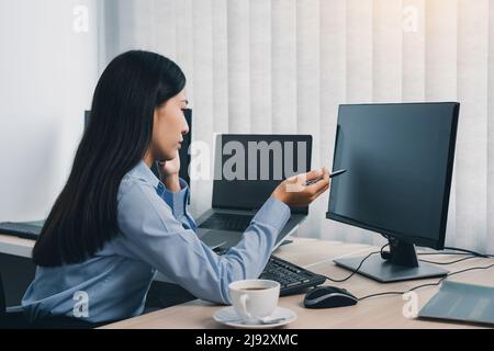 Concentrated asian woman brainstorming while coding data on desktop PC while working on computer codes in the office. Stock Photo