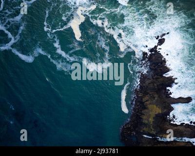 Shot from the air. Turquoise ocean water with white foamy waves and a piece of rocky shore. Seascape. Abstraction. Nature background. Wallpaper. Textu Stock Photo