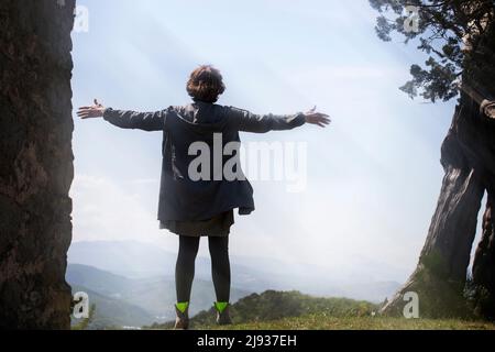 A young woman stands on top of a mountain with her arms outstretched in the wind in the sun. The concept of freedom and purification. Stock Photo