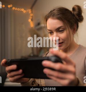 Girl gamer plays a video game on a portable game console. He looks at the screen intently. Close-up. Young people play adventure video games. Prizes, Stock Photo