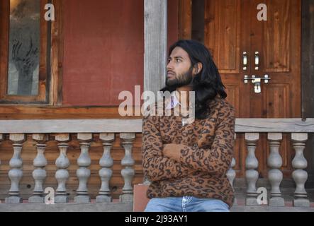 Front view a good looking long haired young guy looking sideways while sitting in old temple posing with crossed arms Stock Photo