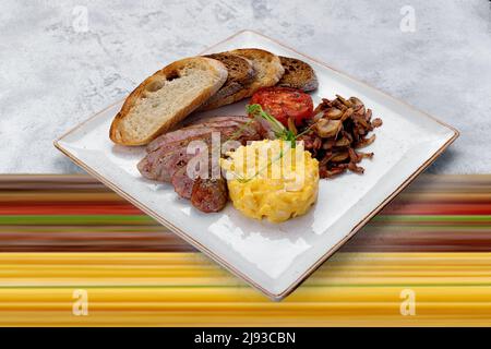 Irish breakfast on a plate. Sausage, scrambled eggs, mushrooms, bacon, ciabatta toast. On a mixed background Stock Photo