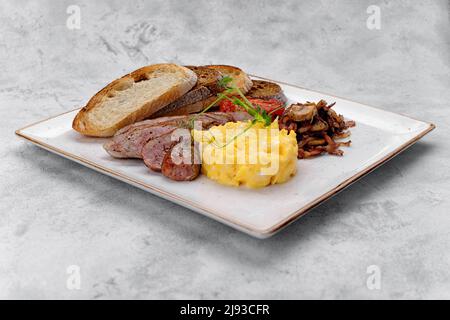 Irish breakfast on a plate. Sausage, scrambled eggs, mushrooms, bacon, ciabatta toast. On a light background Stock Photo
