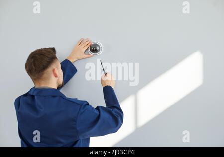 Technician installing modern surveillance CCTV dome camera on wall inside the house Stock Photo