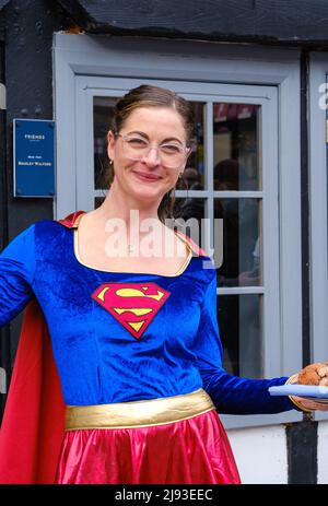 Staff member from Friends Restaurant dressed in Superwoman fancy dress smiles & holds tray of food at 2022 St George’s Day Celebration, Pinner, London Stock Photo