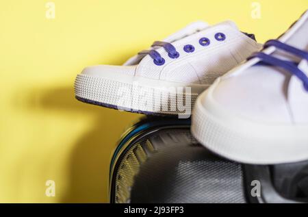 Close up of a suitcase and white sneakers on a yellow background Stock Photo