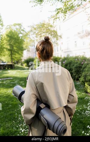back view of woman in trench coat walking on street of european city ...