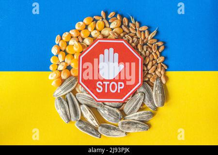 Wheat grains, corn and sunflower seeds on the yellow and blue flag of Ukraine with stop sign, Ukrainian grain crisis, global hunger crisis concept Stock Photo