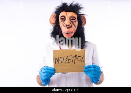 Person dressed in a monkey with a mask, with a medical nurse's suit, with a sign that reads: 'MONKEYPOX', and a syringe, on a white background. Pandem Stock Photo