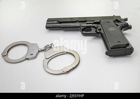 Black handgun and handcuffs flat on a white background. Copy Space. Stock Image. Stock Photo