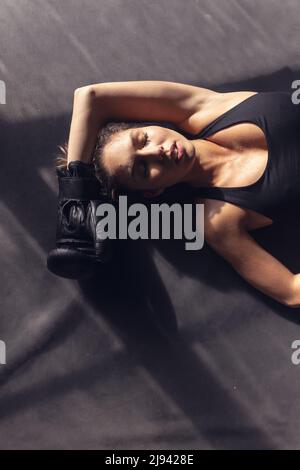 High angle view of caucasian young female tired boxer with eyes closed lying in boxing ring Stock Photo