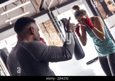 African american male coach teaching boxing to caucasian young female boxer in health club Stock Photo