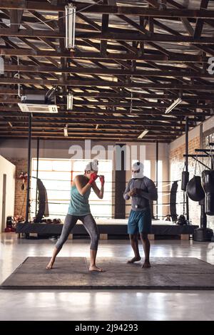African american young male coach guiding while giving training to caucasian young female boxer Stock Photo