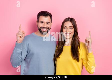 Portrait of two positive friendly partners indicate finger up empty space isolated on pink color background Stock Photo