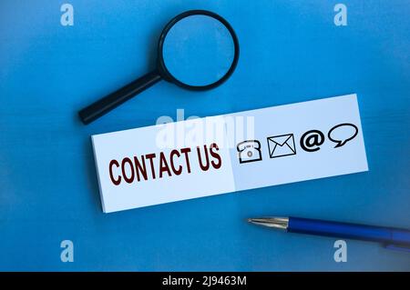 Contact us text with icons on notepad on blue background. Business and communication concept Stock Photo