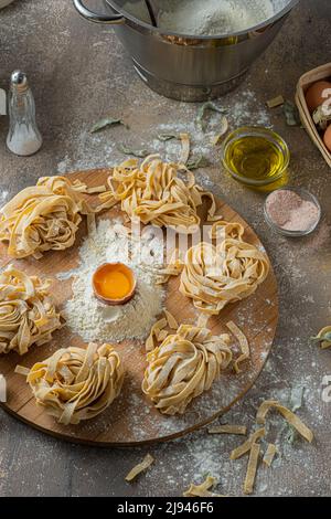 Freshly made tagliatelle pasta with eggs and flour on wooden board Stock Photo