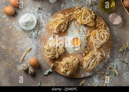 Freshly made tagliatelle pasta with eggs and flour on wooden board Stock Photo