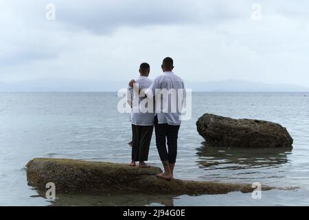 Back of a gay couple standing on a rock looking out to the horizon of the ocean Stock Photo