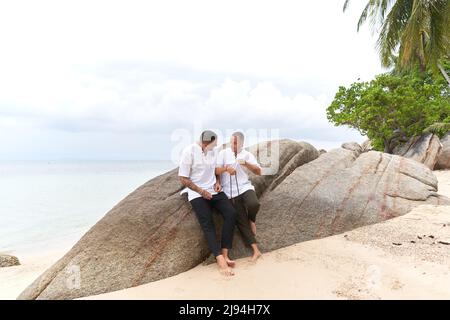 gay couple in white clothes talking on a rock beside the sea Stock Photo