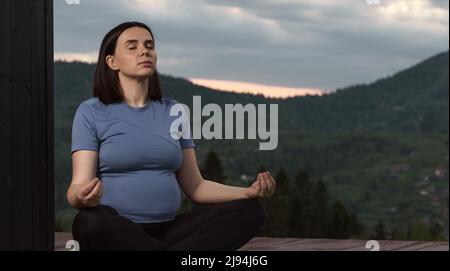 Pregnant woman practicing Yoga outdoor on a terrace with mountain view at sunset time Stock Photo