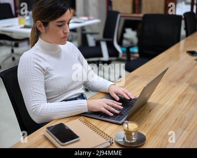woman in a workspace using her computer with a coffee next to it Stock Photo