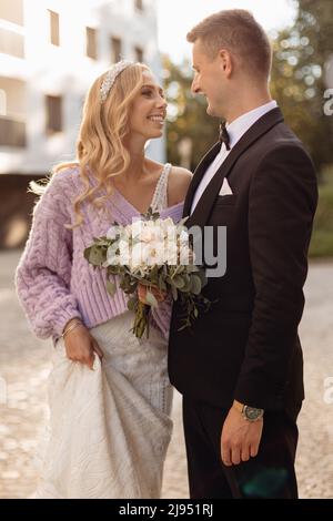 Beautiful wedding couple in black suit and white dress walk around city, laugh and rejoice on street background. Portrait of happy bride with bouquet Stock Photo