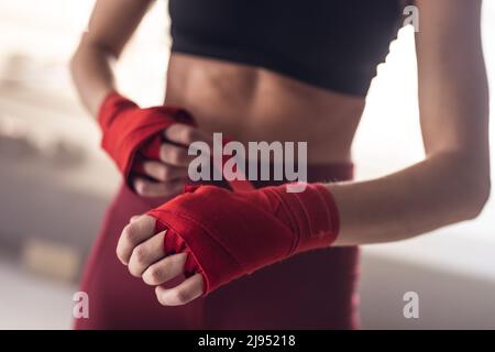 Midsection of caucasian young female boxer wrapping hands with red boxing wraps in health club Stock Photo